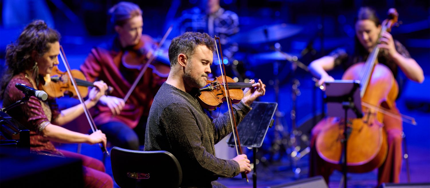 Gruppe von Musikern spielt auf Streichinstrumenten auf einer Bühne mit blauem Hintergrundlicht