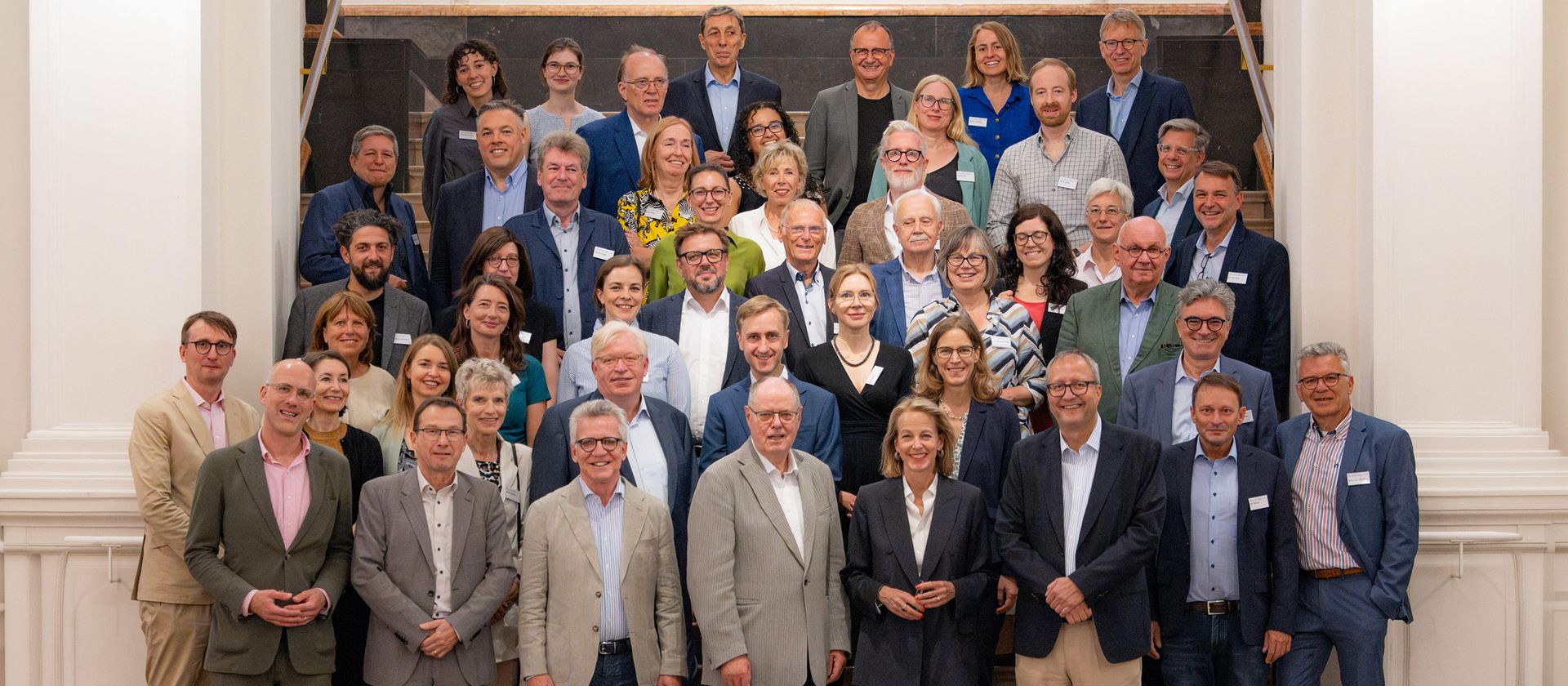 Gruppenfoto von mehreren Personen in einem Treppenhaus, die in die Kamera lächeln