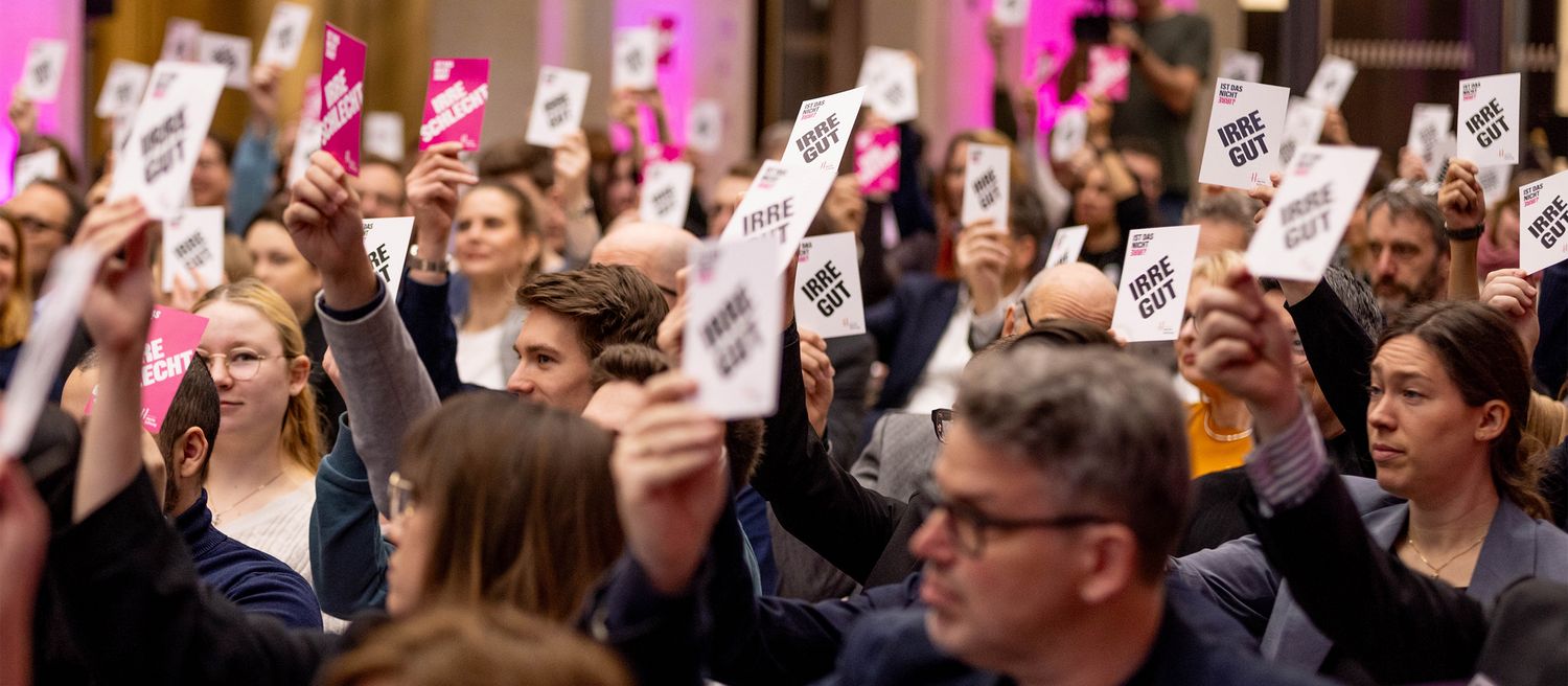 Gruppe von Menschen, die jeweils ein Schild mit der Aufschrift 'IRRE GUT' oder 'BESTE RECHT' hochhalten