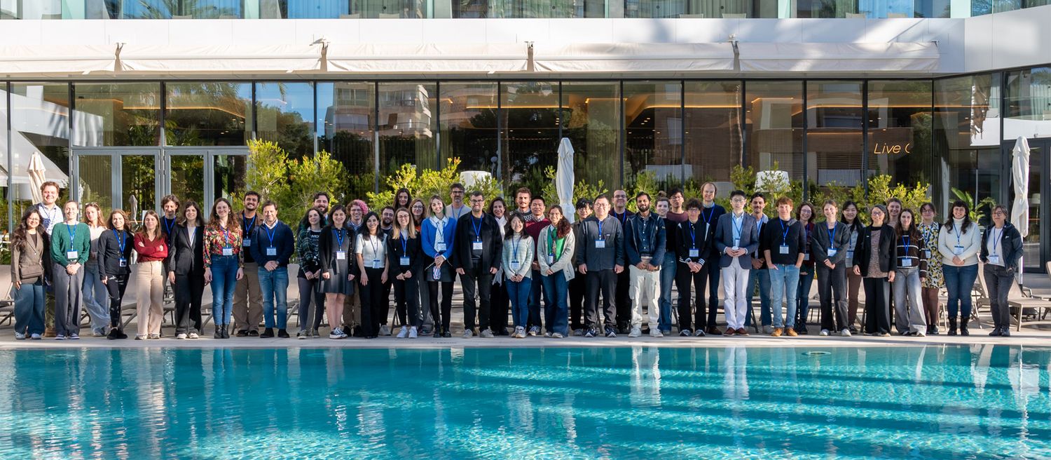 Große Gruppe von Menschen mit Namensschildern steht vor einem Gebäude mit großen Glasfenstern und einem Pool im Vordergrund